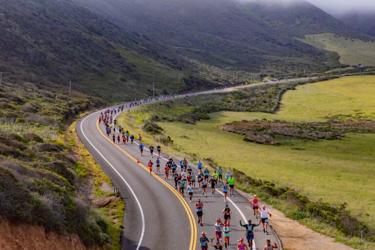 Photo of runners passing through beautiful green scenery at the Big Sur Marathon 2024