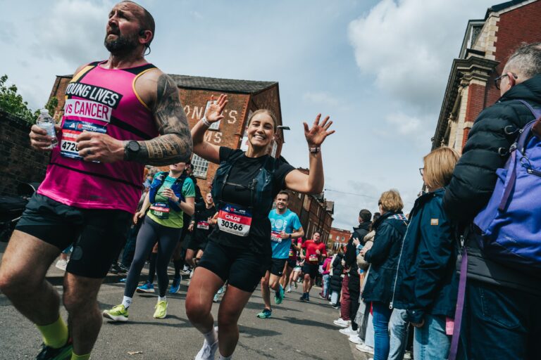 A runner waves at the camera during the Manchester Marathon 2025