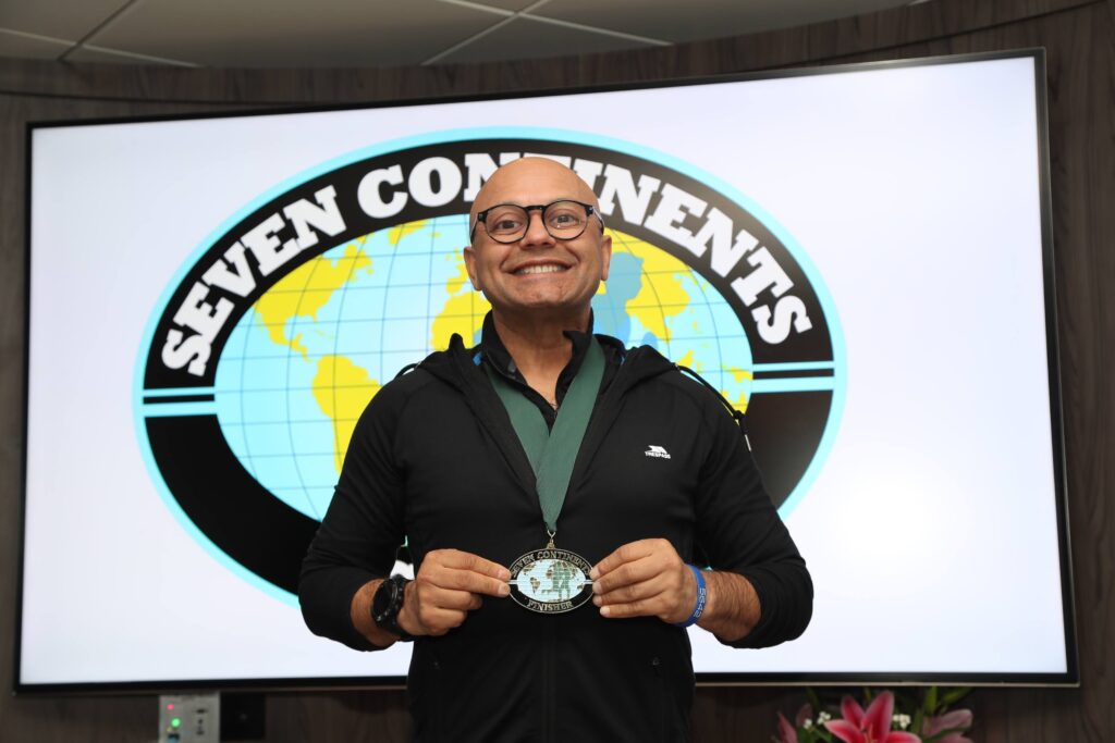 A runner poses in front of the Seven Continents Club banner with their medal