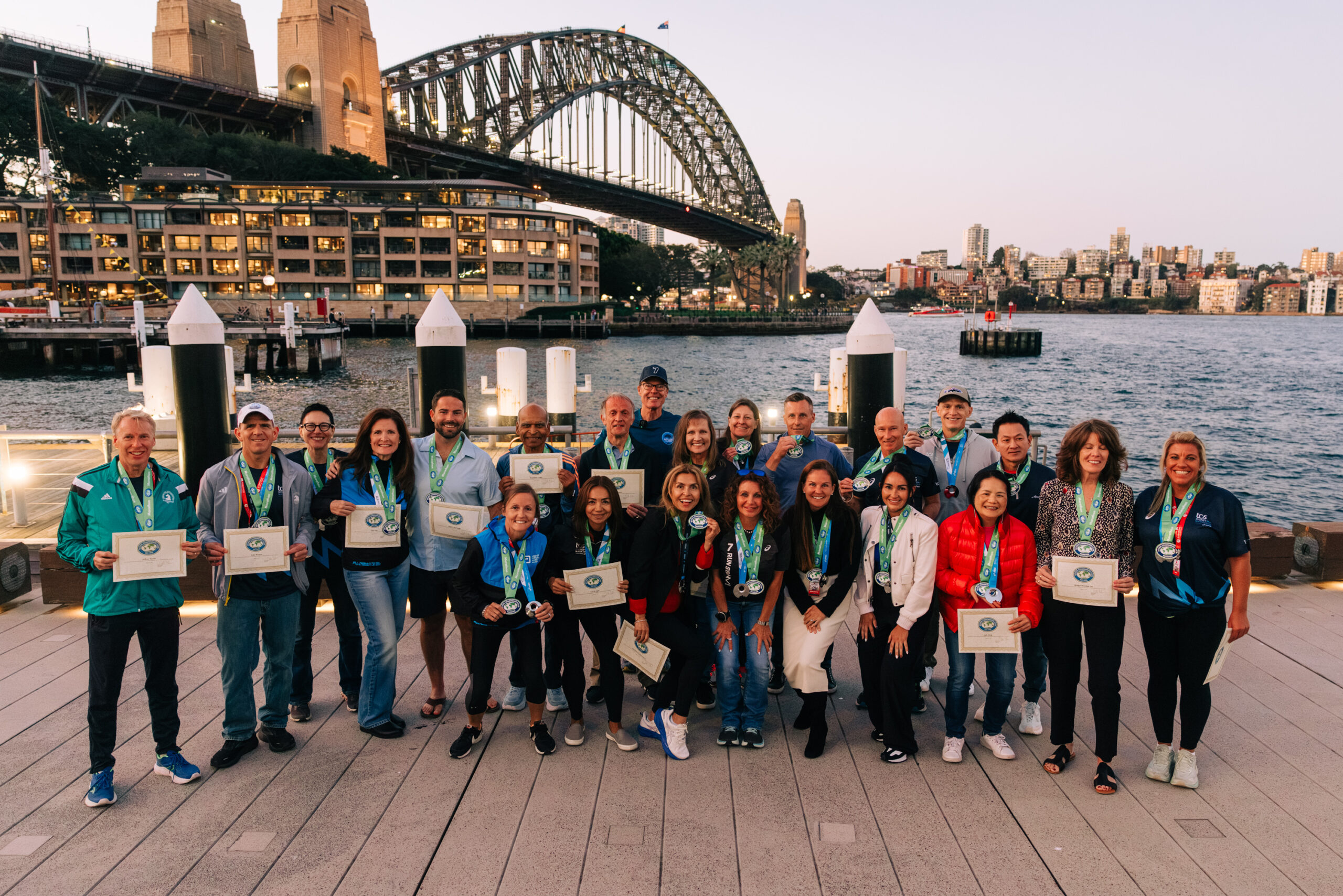 Runners pose with their Seven Continents Club medals and certificates beneath the Sydney Harbour Bridge