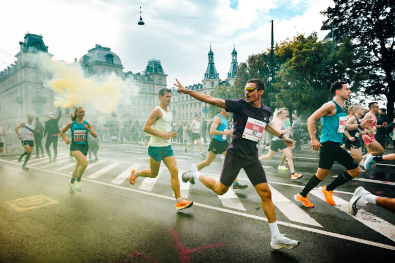 A runner passing through flare-lined streets during the Copenhagen Half Marathon 2027