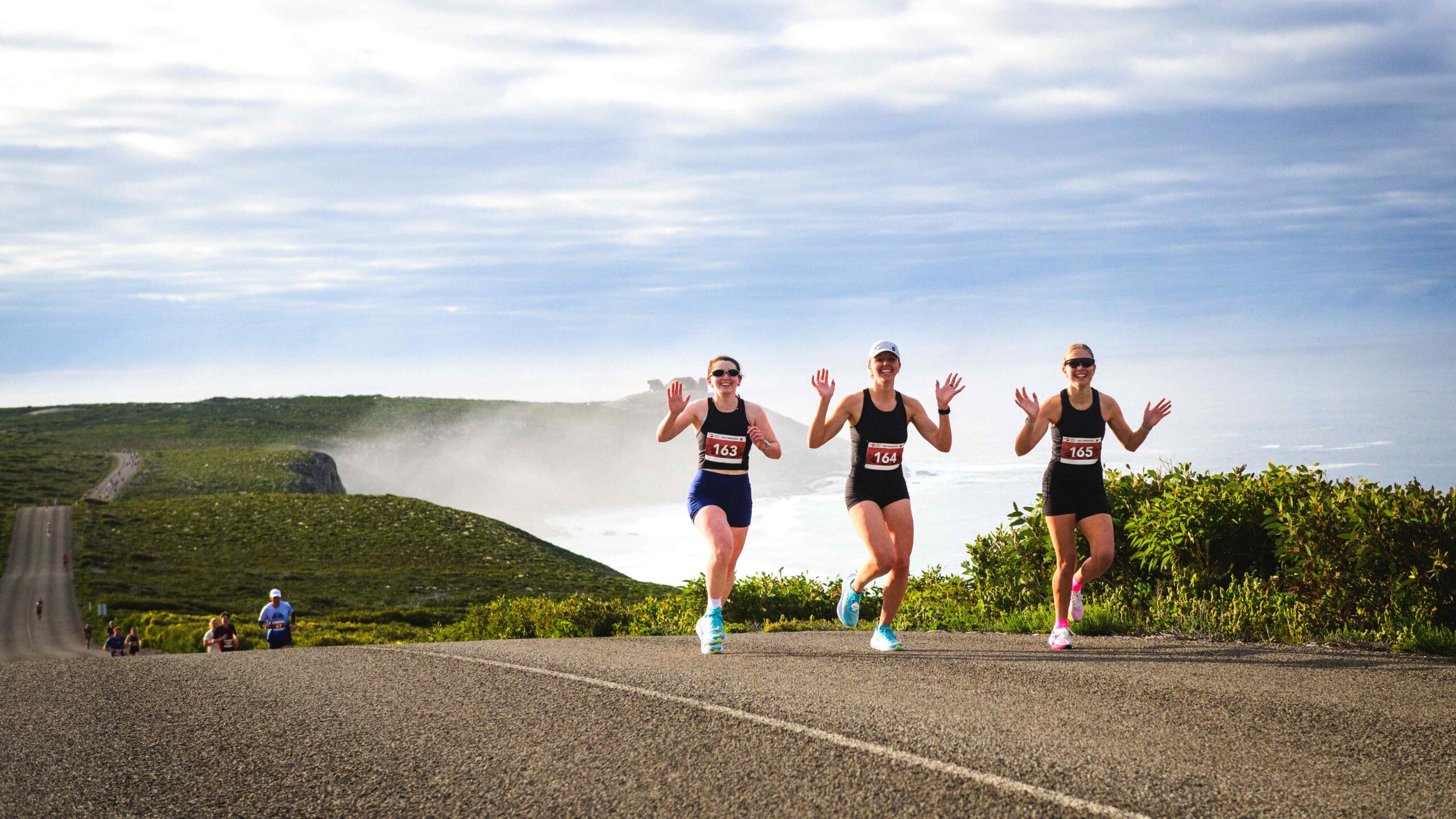 Three female runners hold their arms aloft as they take part in the Kangaroo Island Marathon